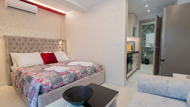 Une chambre moderne avec une tête de lit capitonnée, un lit avec une literie à motifs, une table de chevet agrémentée d’un bol décoratif et une vue sur la salle de bain.