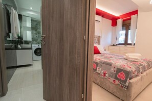 A bedroom with a bed, a nightstand, a dresser, and a window with curtains. - Orestis Suite No 2 by RentalsPro - Nea Moudania (Nea Moudania)