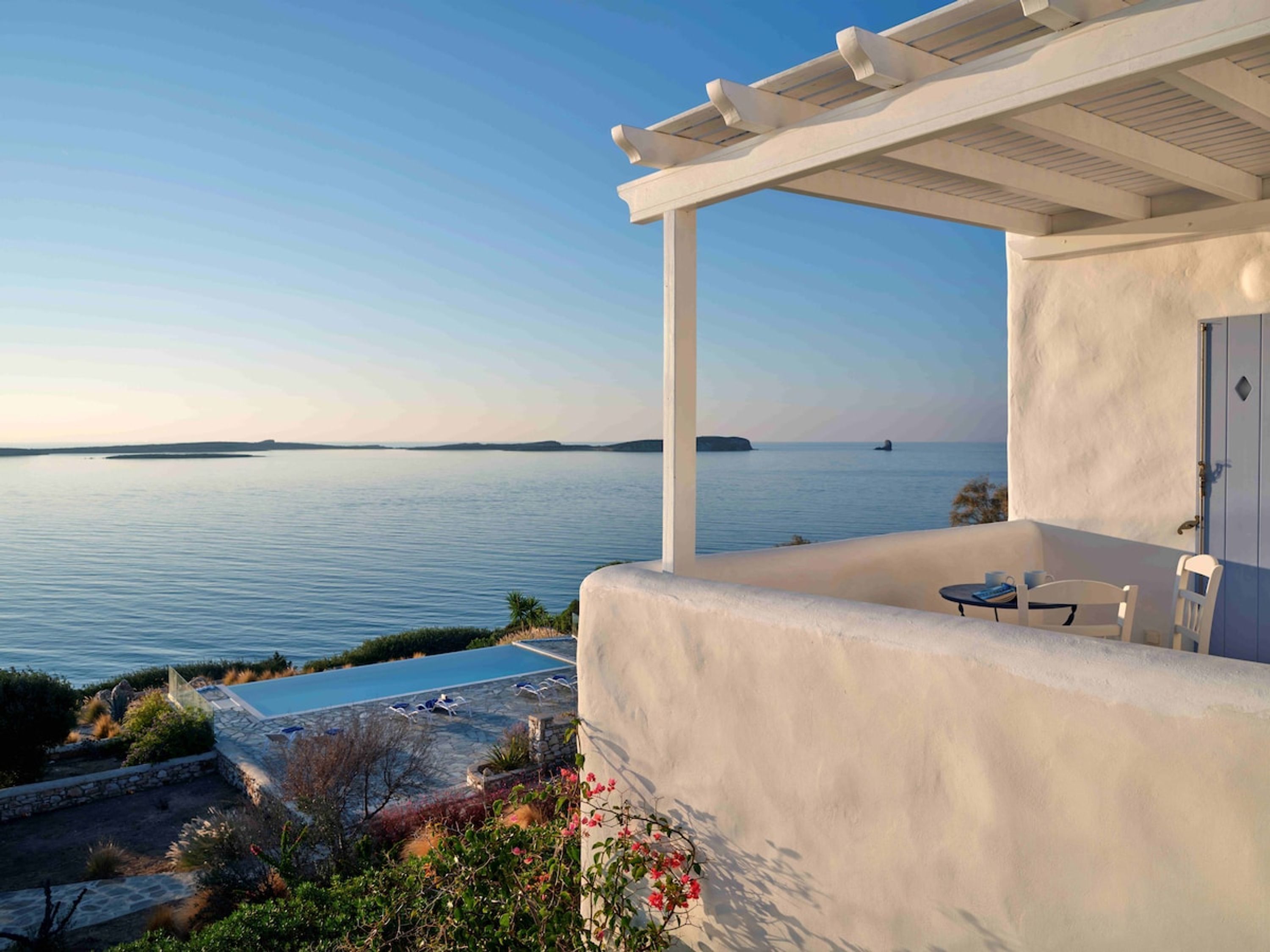 Blick auf das Meer von einer überdachten Außenterrasse mit Pool, einer Pergola und einem Tisch mit Stühlen.