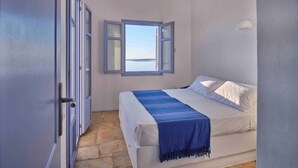 Ein Schlafzimmer mit Bett, Fenster mit geöffnetem Klappladen und Steinboden.