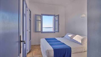 Ein Schlafzimmer mit Bett, Fenster mit geöffnetem Klappladen und Steinboden.