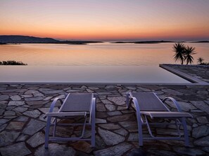 A stone deck with two lounge chairs facing a body of water at sunset. - Seafront Villa Elia -island Living- (Paros)