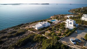En fastighet vid kusten med vita byggnader, en swimmingpool och en parkeringsplats.