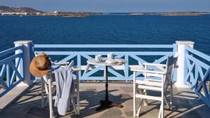 En terrass vid havet med vita stolar, ett bord och en hatt, med utsikt över havet.