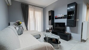 A modern living room with a sofa, a TV, a coffee table, and a window with curtains. - Sweet Home by RentalsPro - Nea Moudania (Nea Moudania)
