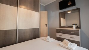 A hotel room with a bed, a dresser, a mirror, and a TV. - Sweet Home by RentalsPro - Nea Moudania (Nea Moudania)