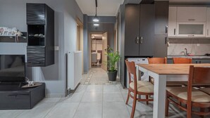A modern kitchen with grey cabinets, a dining area with a wooden table and chairs, and a hallway leading to a bathroom. - Sweet Home by RentalsPro - Nea Moudania (Nea Moudania)
