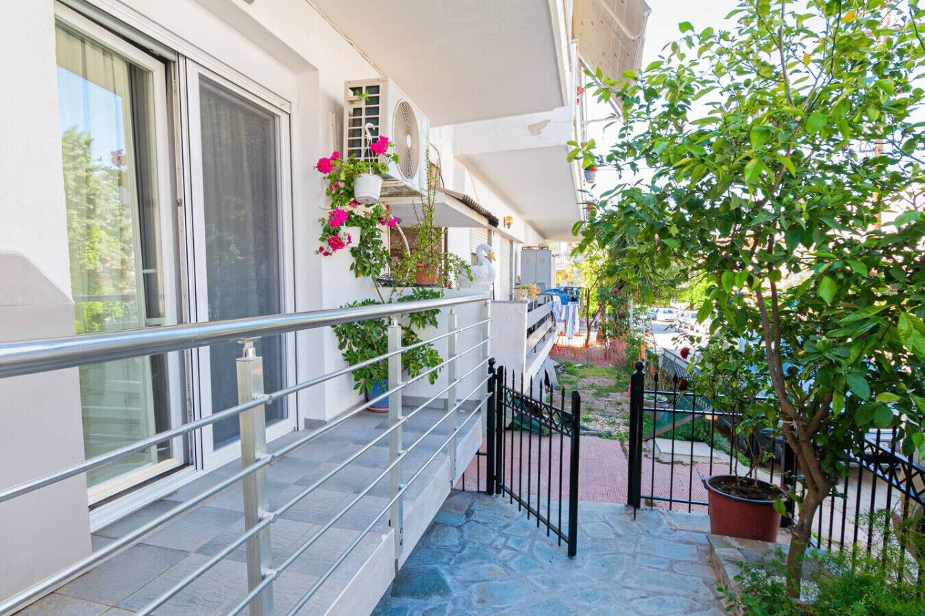 A balcony with a metal railing, potted plants, and a small tree.