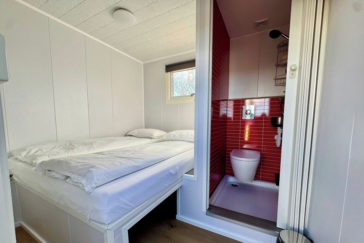 Ein kleines Zimmer mit einem Bett, einem kleinen Fenster und einem Badezimmer mit roten Fliesen.