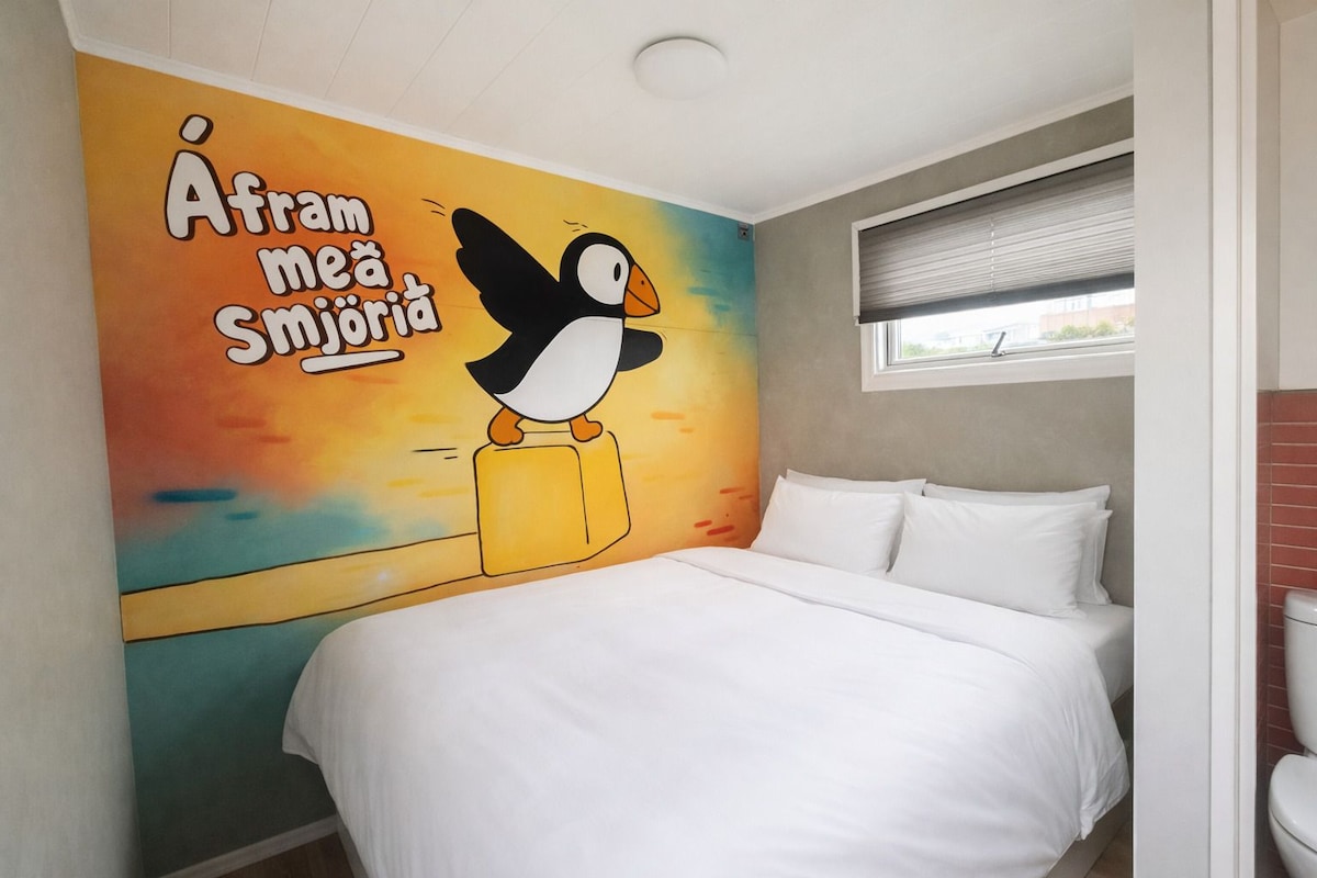 Un dormitorio con cama, un mural en la pared, una ventana y un inodoro.