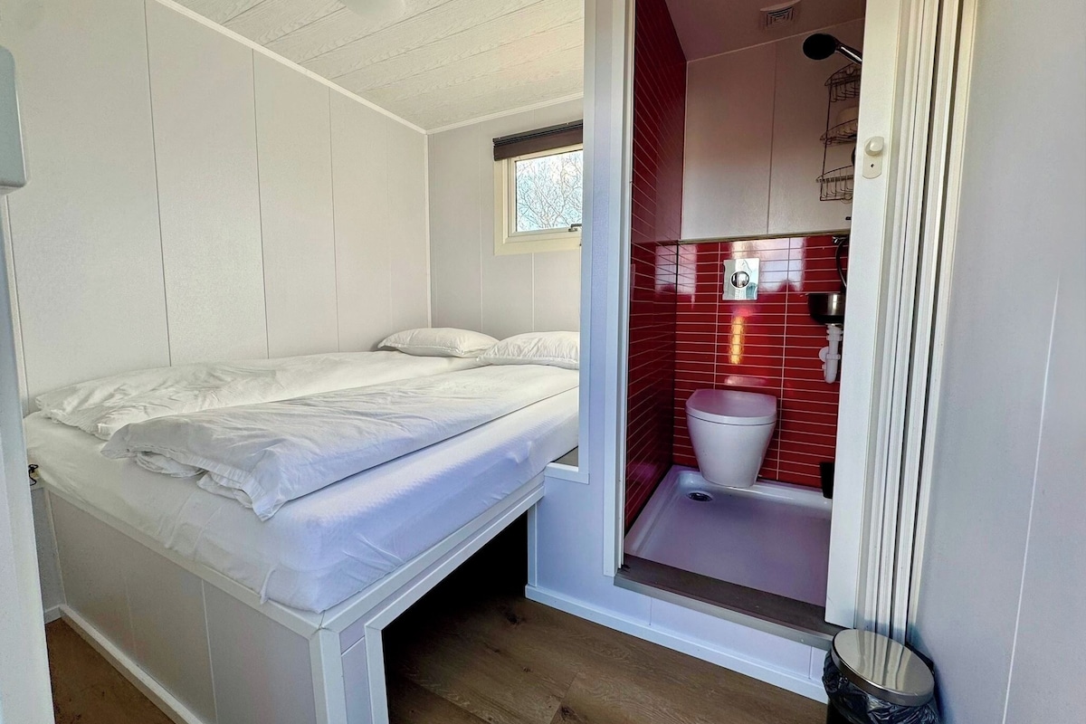 Habitación pequeña con cama, un ventanal y un baño con azulejos rojos.