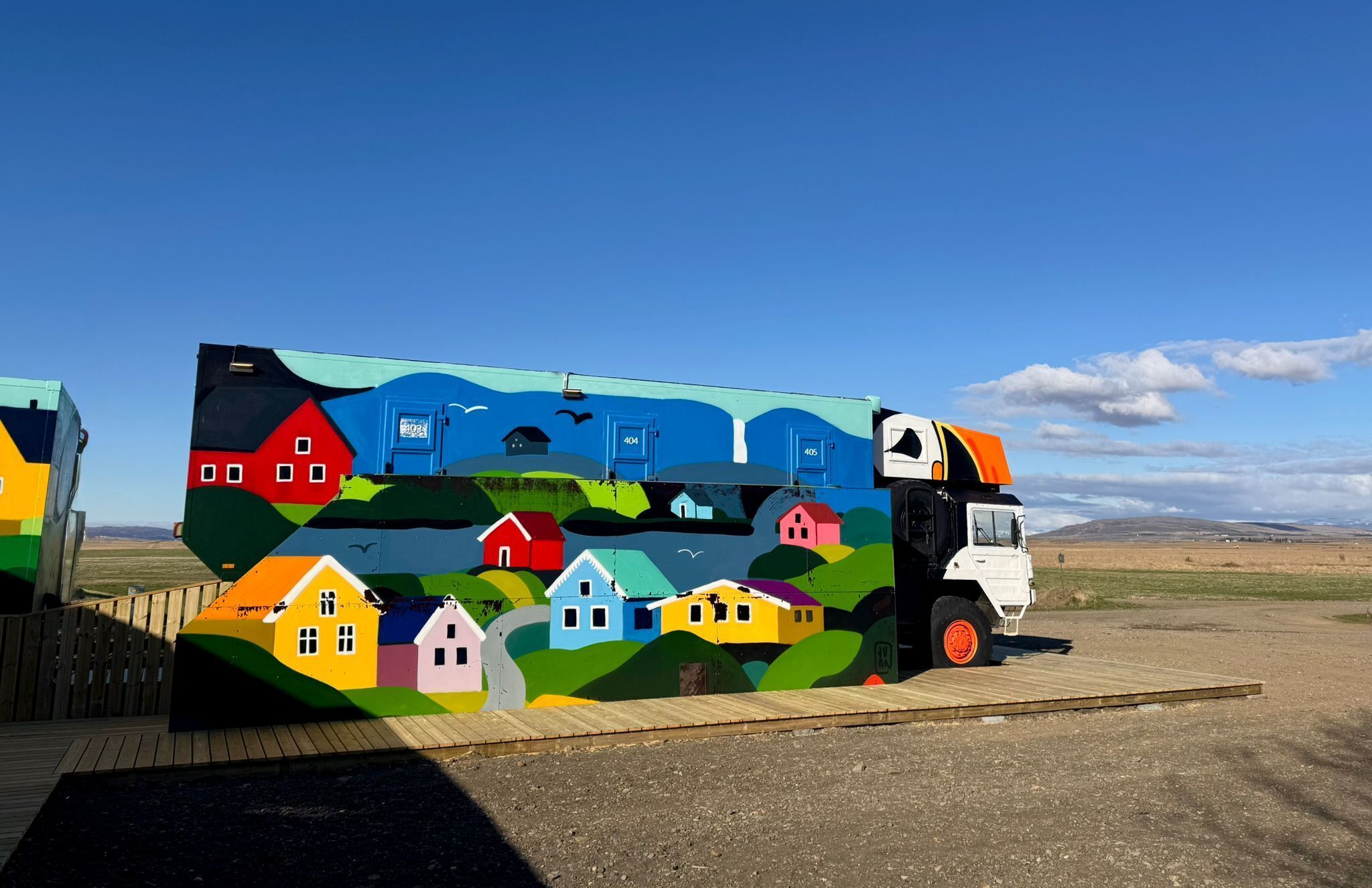 A colorful bus with a house-themed mural, parked on a wooden platform.