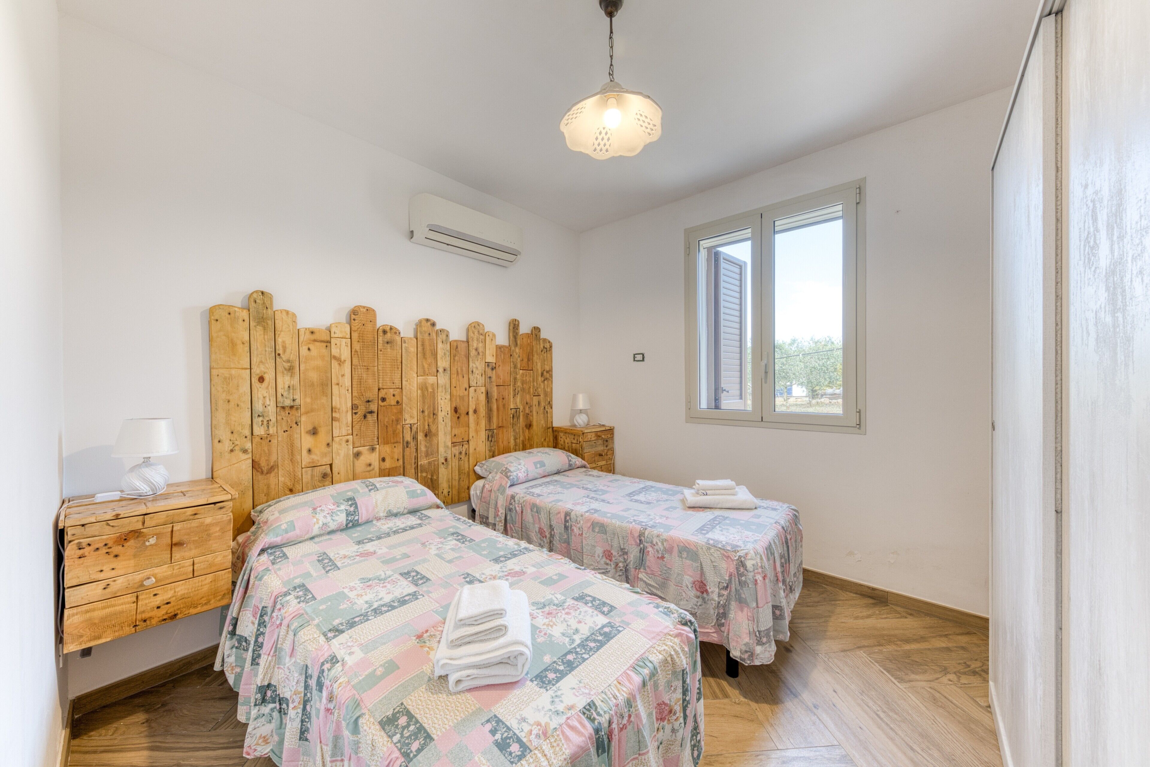 Un dormitorio con dos camas, cabeceros de madera, mesitas de noche y una ventana.