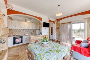 Una cocina con armarios blancos, una mesa de comedor con mantel estampado de frutas y un sofá rojo.