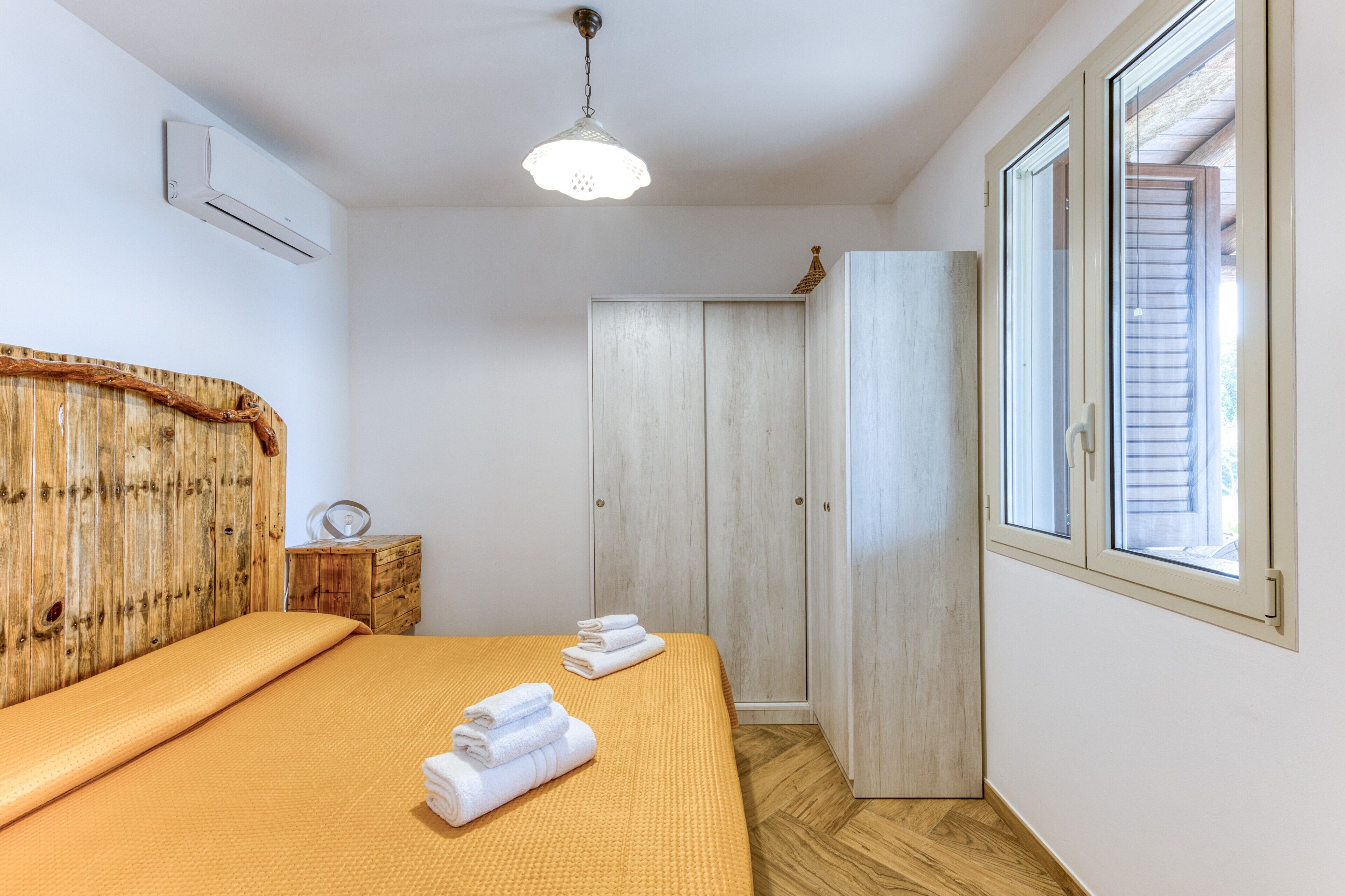 A bedroom with a bed, a wooden headboard, a wardrobe, and a window.