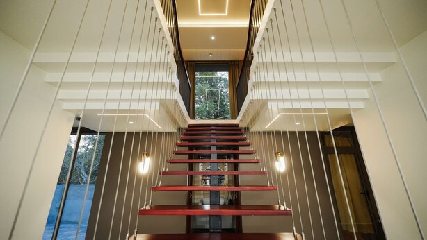 A modern staircase with a central column, glass railings, and recessed lighting. - Sukoon By Spynora (Vythiri)