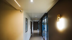 A hallway with a camera, recessed lighting, and a wall-mounted light fixture. - Sukoon By Spynora (Vythiri)