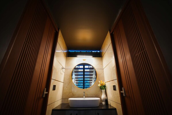 A bathroom with a round mirror, a white sink, and a vase with flowers. - Sukoon By Spynora (Vythiri)