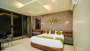 A modern hotel room with a large bed, a glass door leading to a balcony, a wooden headboard, and a wall-mounted light fixture. - Sukoon By Spynora (Vythiri)