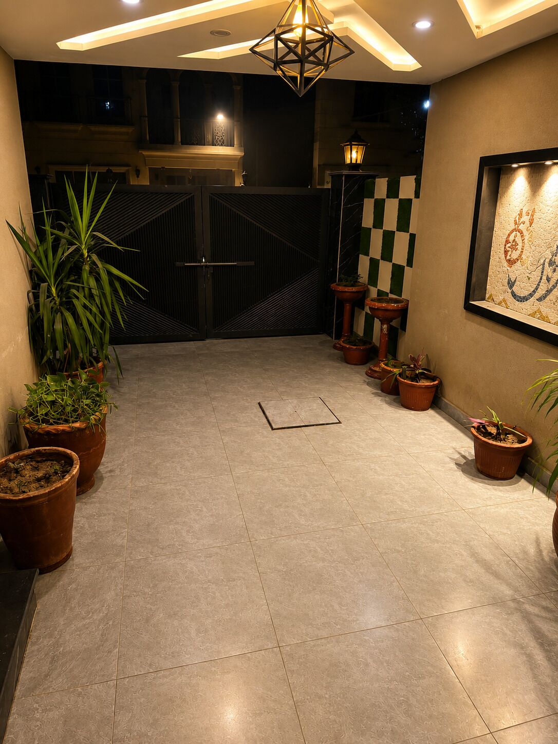 Un intérieur moderne avec un luminaire au plafond aux motifs géométriques, un mur à carreaux et des plantes en pot.