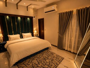 Een slaapkamer met een bed, nachtkastjes, een lamp, een airconditioner en een gordijn.