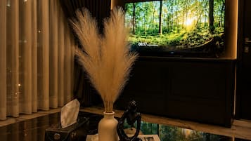 Un intérieur moderne avec un grand téléviseur à écran plat diffusant une scène de forêt, un vase contenant de l’herbe des pampas, une télécommande et un livre intitulé « VIVEZ PLEINEMENT ».