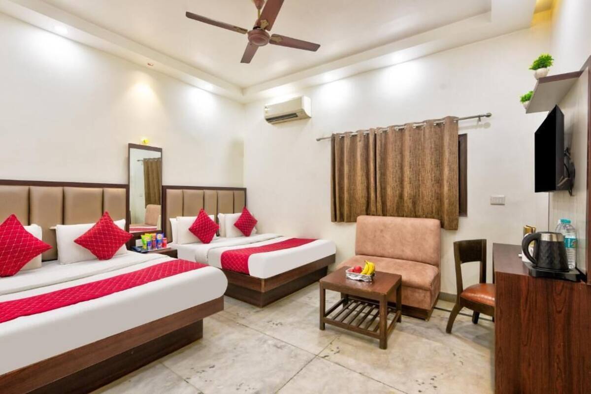 A hotel room with two beds, a sofa, a coffee table, a TV, and a ceiling fan.