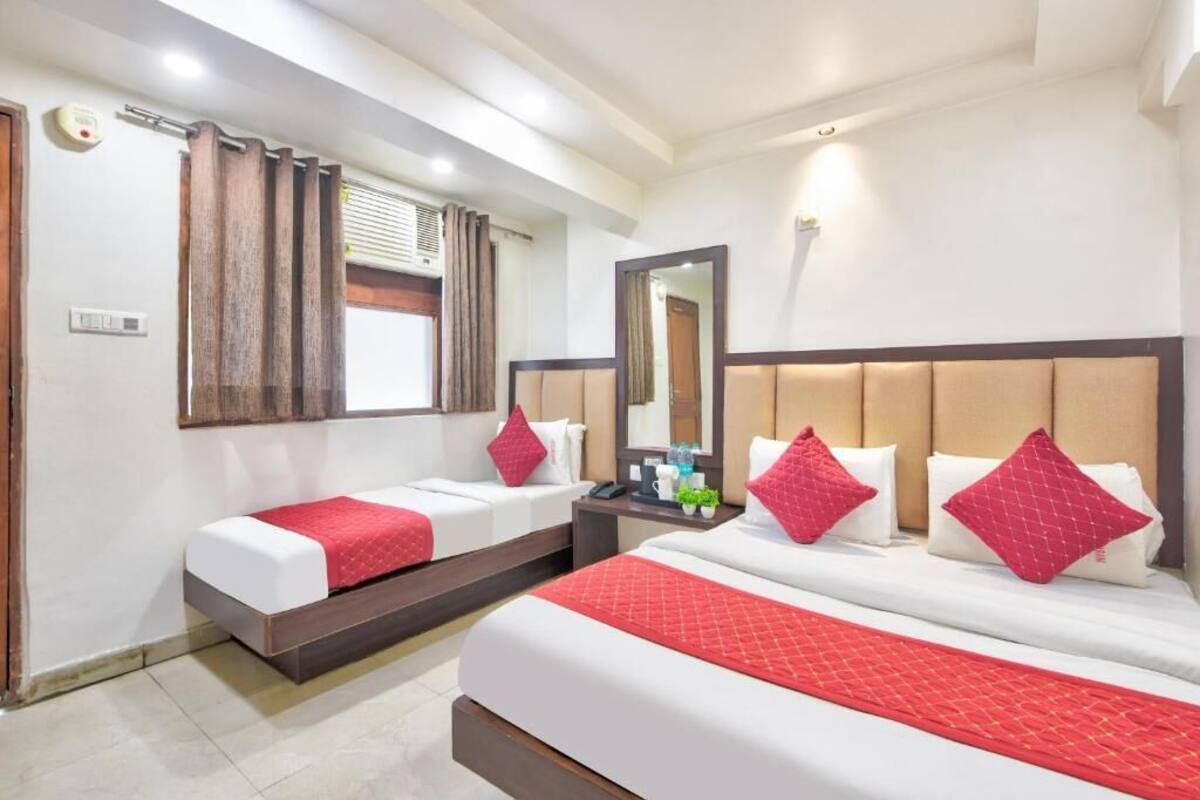 A hotel room with two beds, a nightstand, a mirror, and a window with curtains.