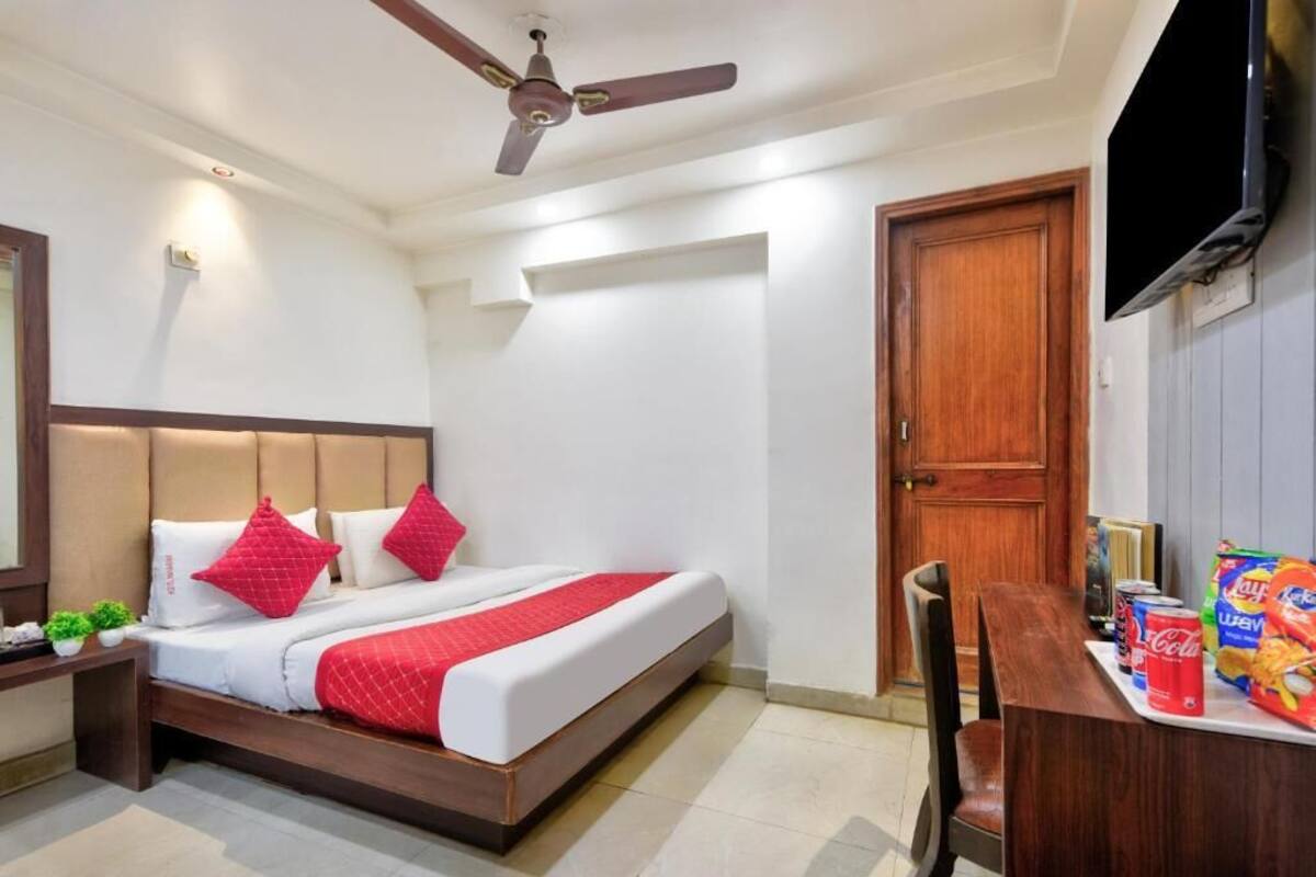A hotel room with a bed, a desk with snacks, a TV, and a ceiling fan.