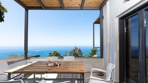 An outdoor patio with a wooden table and white chairs, overlooking a scenic ocean view. - Anemos Luxury Villas (Agios Vasileios)