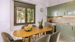 A dining area with a wooden table, chairs, a bowl of fruit, and a potted plant. - Anemos Luxury Villas (Agios Vasileios)