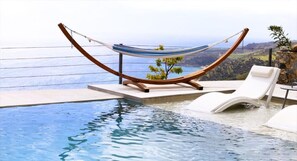 Ein Endlos-Pool mit einer Hängematte und Liegestühlen, mit Blick auf eine malerische Landschaft.