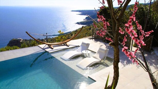 A pool with a hammock and lounge chairs overlooking a coastal view. - Anemos Luxury Villas (Agios Vasileios)