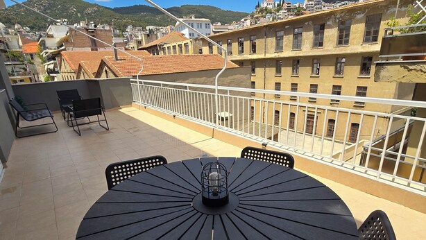 Ein runder Tisch mit Stühlen auf einem Balkon, mit Blick auf Gebäude und Berge.