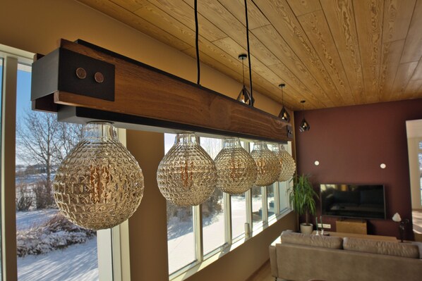 A modern living room with a wooden ceiling, large windows, and a television. - Ægissíða - Renovated Country House (Hella)