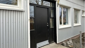 Un edificio con puerta negra, ventanas con marco blanco y fachada de metal corrugado.