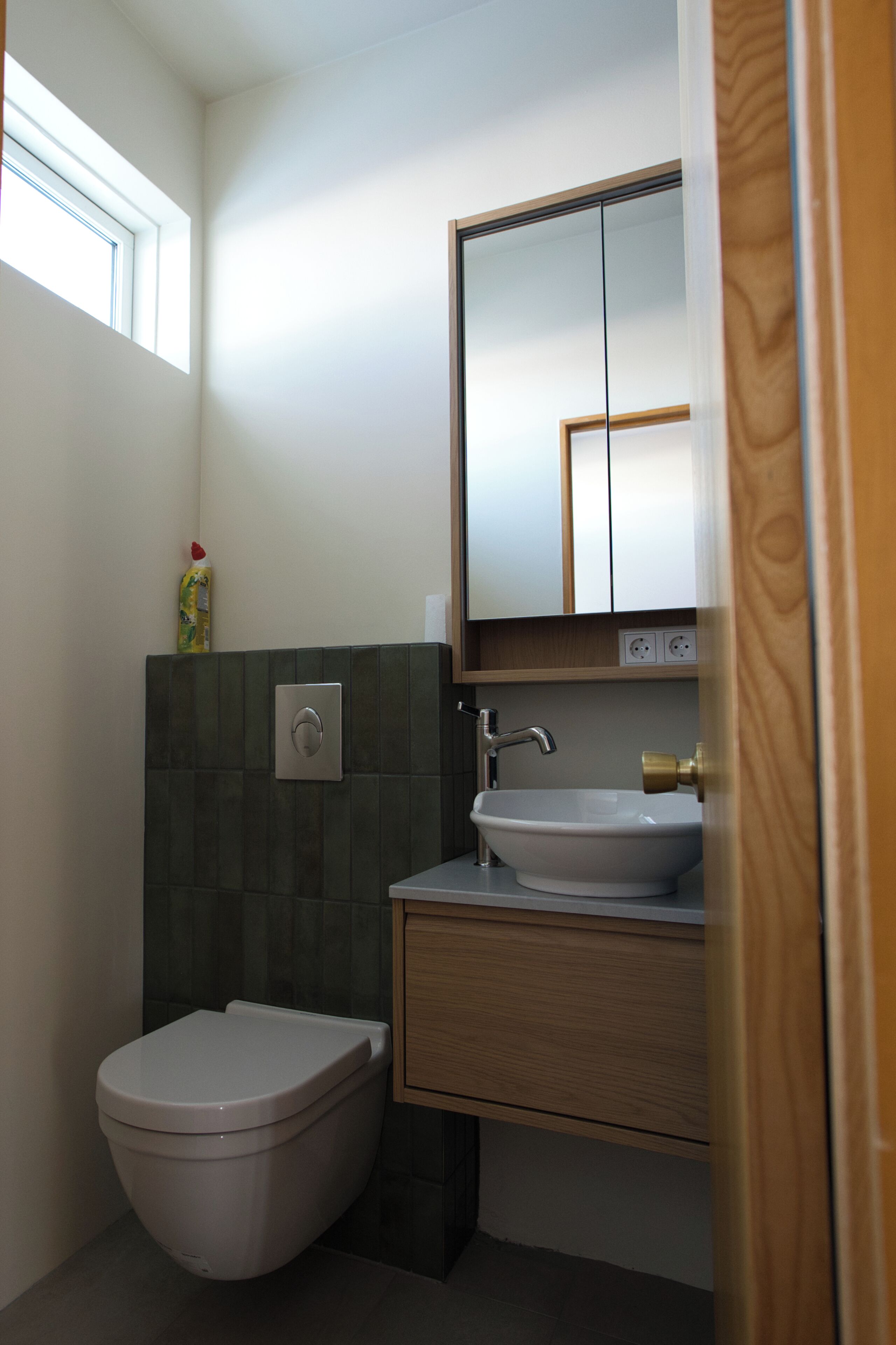 A bathroom with a toilet, sink, mirror, and a window.