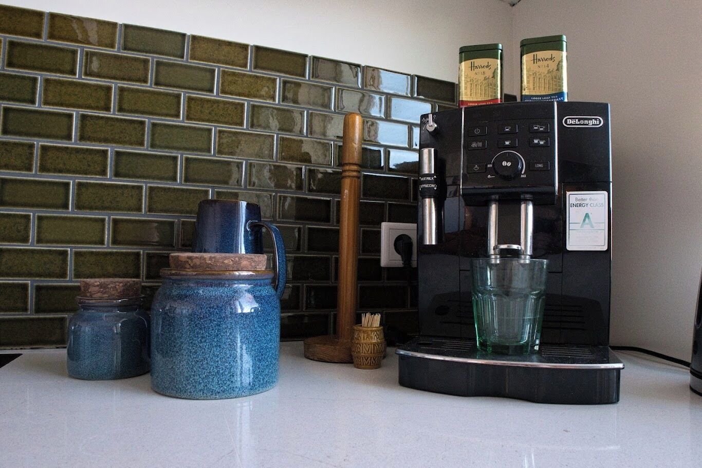 A kitchen counter with a coffee maker, jars, and a wooden spoon.