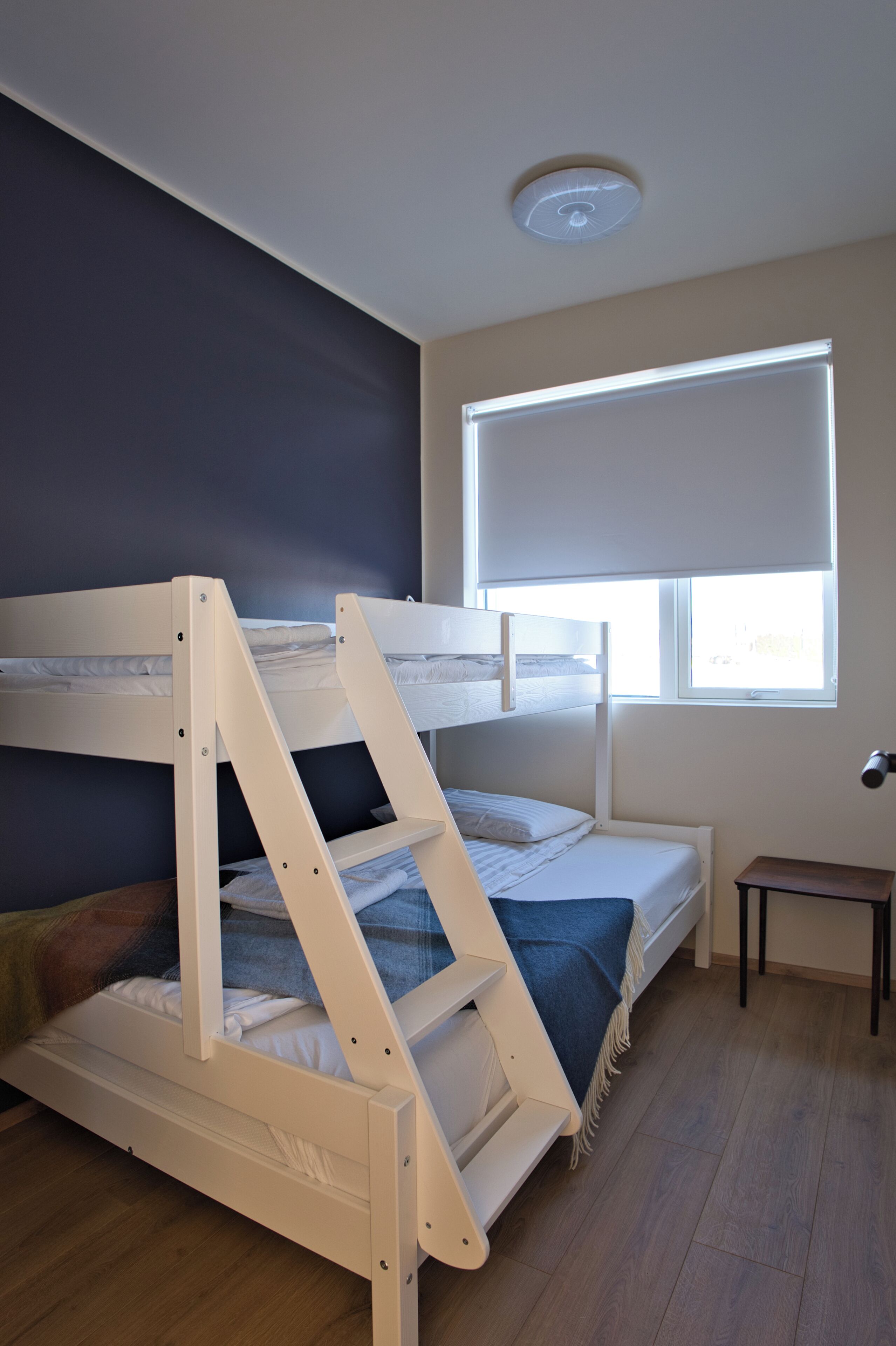 En køjeseng med et vindue over, et lille bord og en loftlampe.