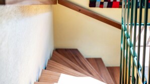 Eine Holztreppe mit Metallgeländer, die zu einem Raum mit weißer Wand und einer farbenfrohen Stegdecke führt.
