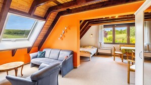 Ein Zimmer mit schrägem Dach, einer Couch, einem Bett, einem Esstisch und Stühlen.