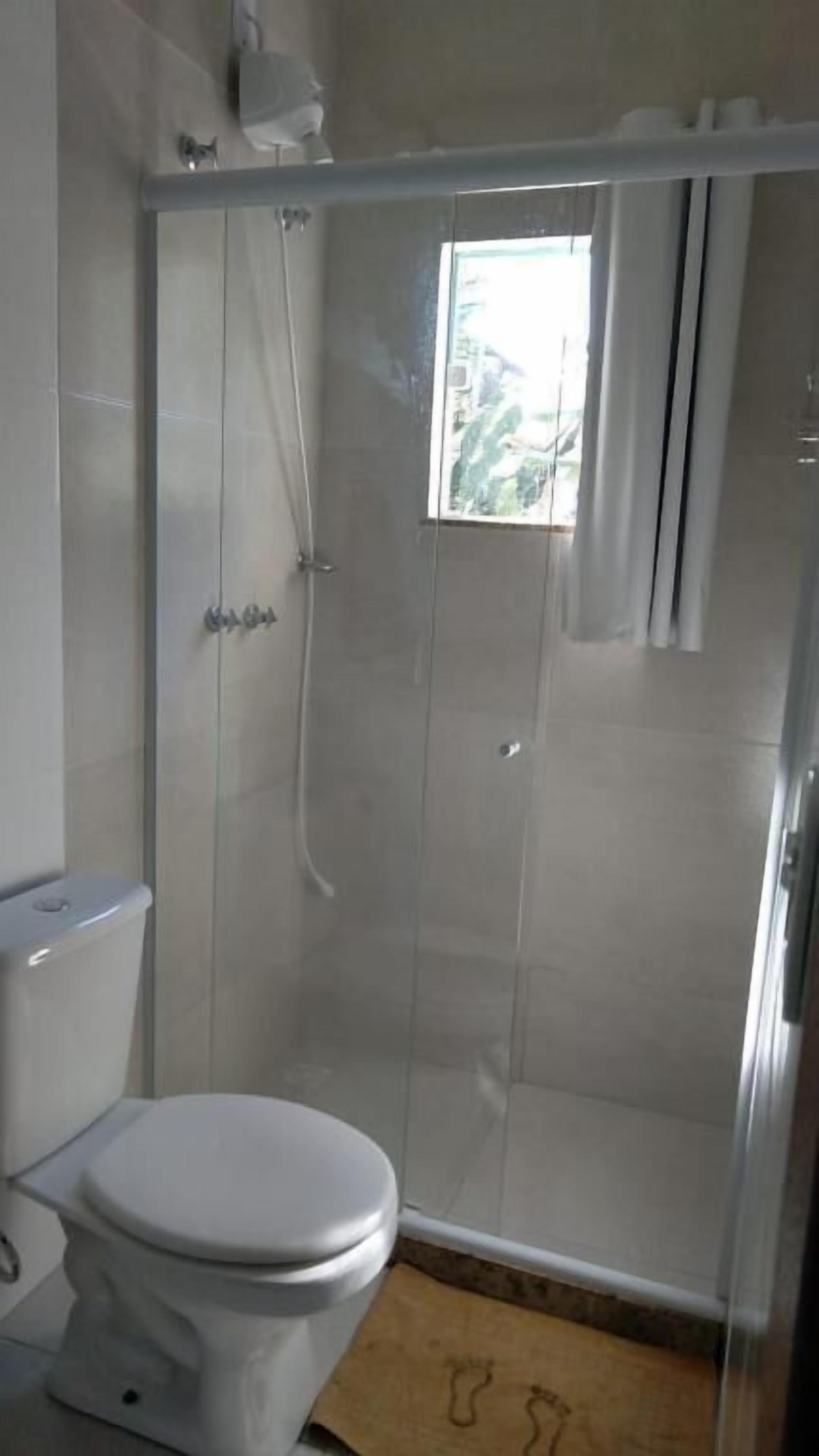 Een badkamer met toilet, douchecabine en raam.