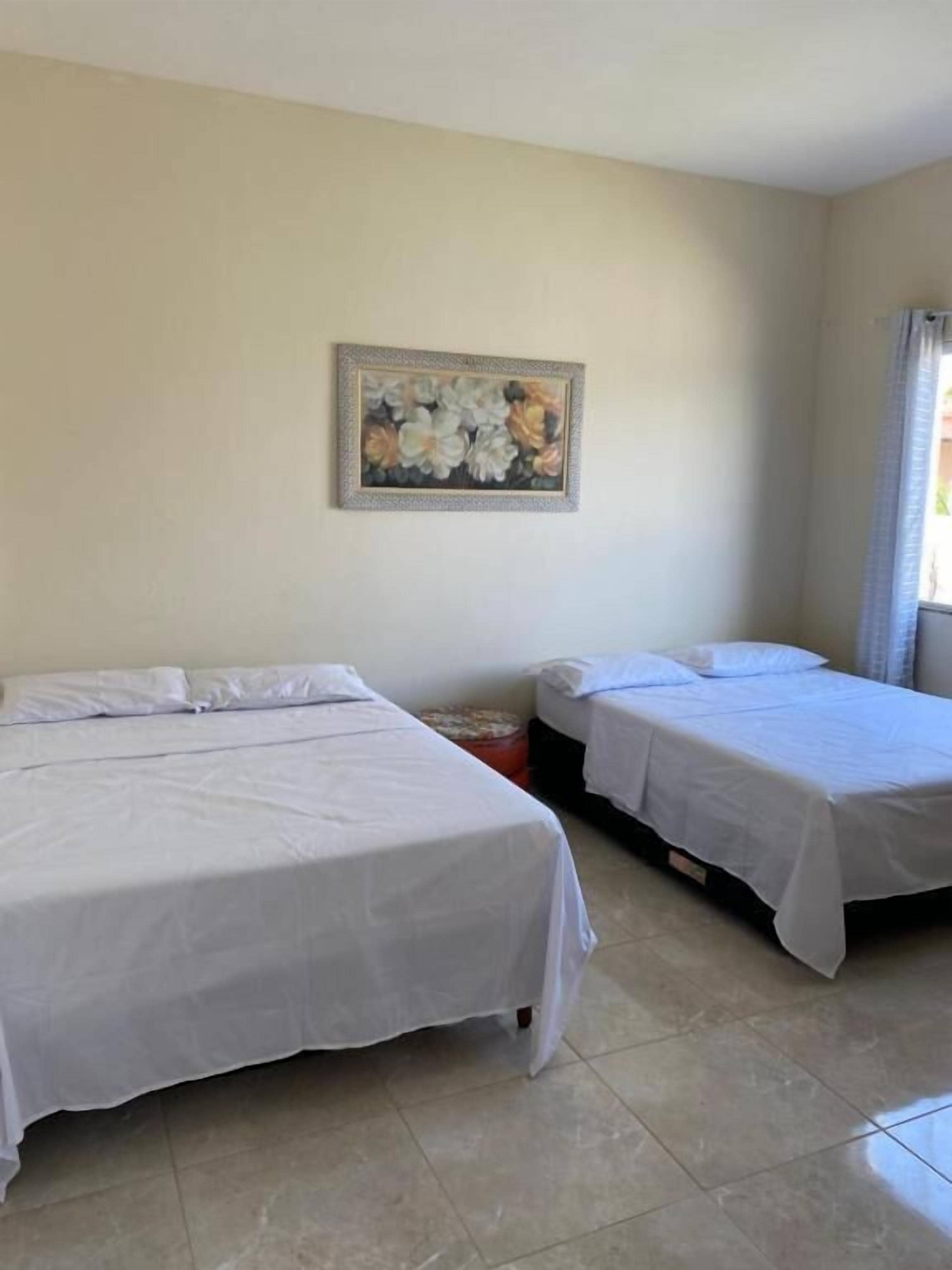 A room with two beds, a painting on the wall, and a tiled floor.
