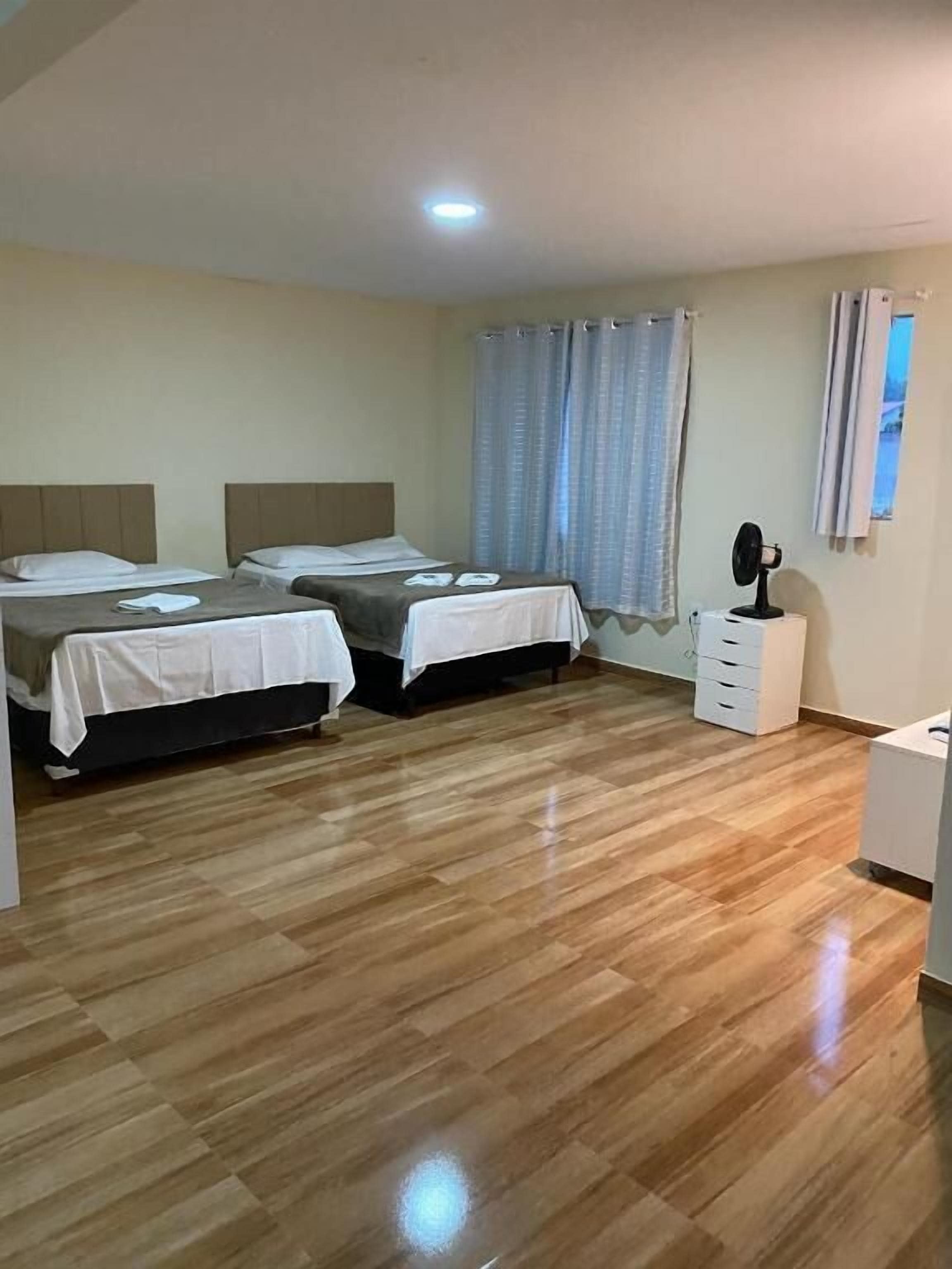 Une chambre d’hôtel avec deux lits, un bureau, une chaise, un miroir et une fenêtre avec des rideaux.