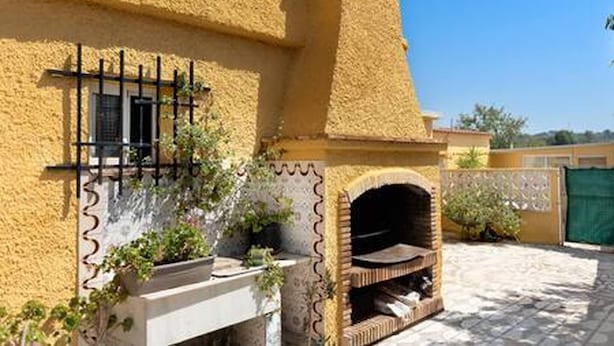 Un bâtiment à l’extérieur jaune et à la texture particulière, doté d’un four en briques et d’une fenêtre ornée de barreaux noirs.