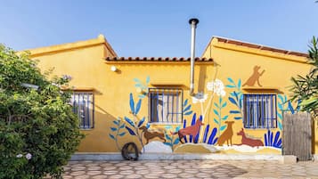 Un edificio amarillo con un mural de animales y plantas, un poste de metal y una cerca de madera.