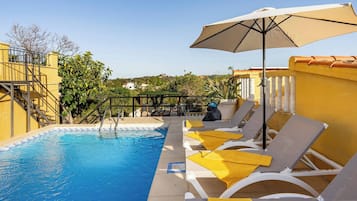 Zona de piscina con sillones de descanso y sombrillas, rodeada de paredes amarillas y vistas despejadas del paisaje.
