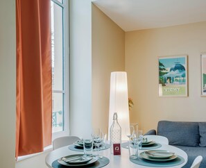 A dining area with a table set for four, a bottle of water, and a poster on the wall. - Very spacious T2 apartment in Vichy's hypercentre, a stone's throw from the thermal baths (Vichy)