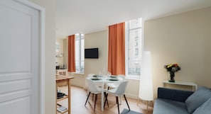 A compact living space with a dining area, a sofa, and a TV mounted on the wall. - Very spacious T2 apartment in Vichy's hypercentre, a stone's throw from the thermal baths (Vichy)