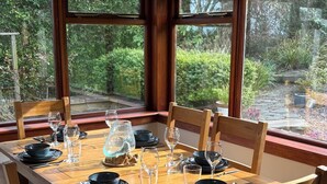A dining table set for six with wooden chairs, positioned near large windows with a view of greenery. - Garden Cottage Near Edinburgh City Centre NEW (Edinburgh)